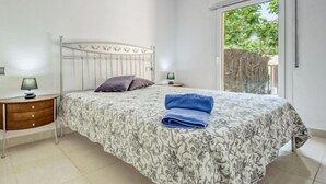 Une chambre à coucher avec un lit en métal, une couvre-lit à motifs, deux oreillers, une serviette bleue, une lampe de chevet et une petite table.