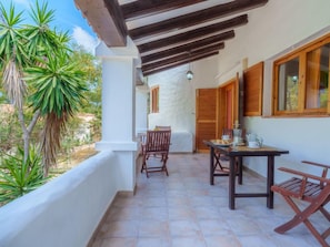 A balcony with a table and chairs, a wooden door, and a view of greenery. - Es Pujols by Interhome (Es Pujols)