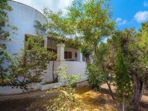 A white building with a curved facade, a small porch, and a garden area with trees and shrubs. - Es Pujols by Interhome (Es Pujols)