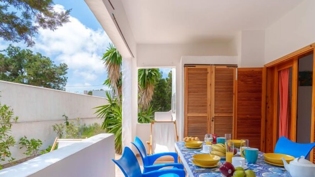 A balcony with a table set for breakfast, blue chairs, and a view of trees and buildings. - Es Pujols by Interhome (Es Pujols)