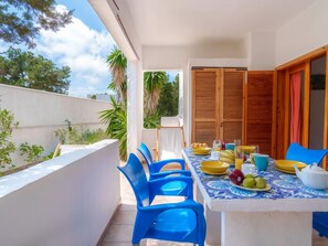 A balcony with a table set for breakfast, blue chairs, and a view of trees and buildings. - Es Pujols by Interhome (Es Pujols)