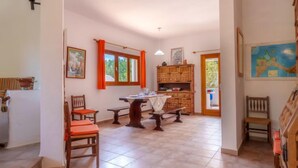 A spacious dining area with a wooden table and chairs, a kitchen with wooden cabinets, and a view of the outdoors through a window. - Es Pujols by Interhome (Es Pujols)