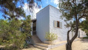 A modern white building with a staircase leading to a door, surrounded by trees and a sandy ground. - Es Pujols by Interhome (Es Pujols)