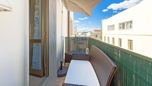 Een balkon met een rieten bank, een tafel en een grote parasol.