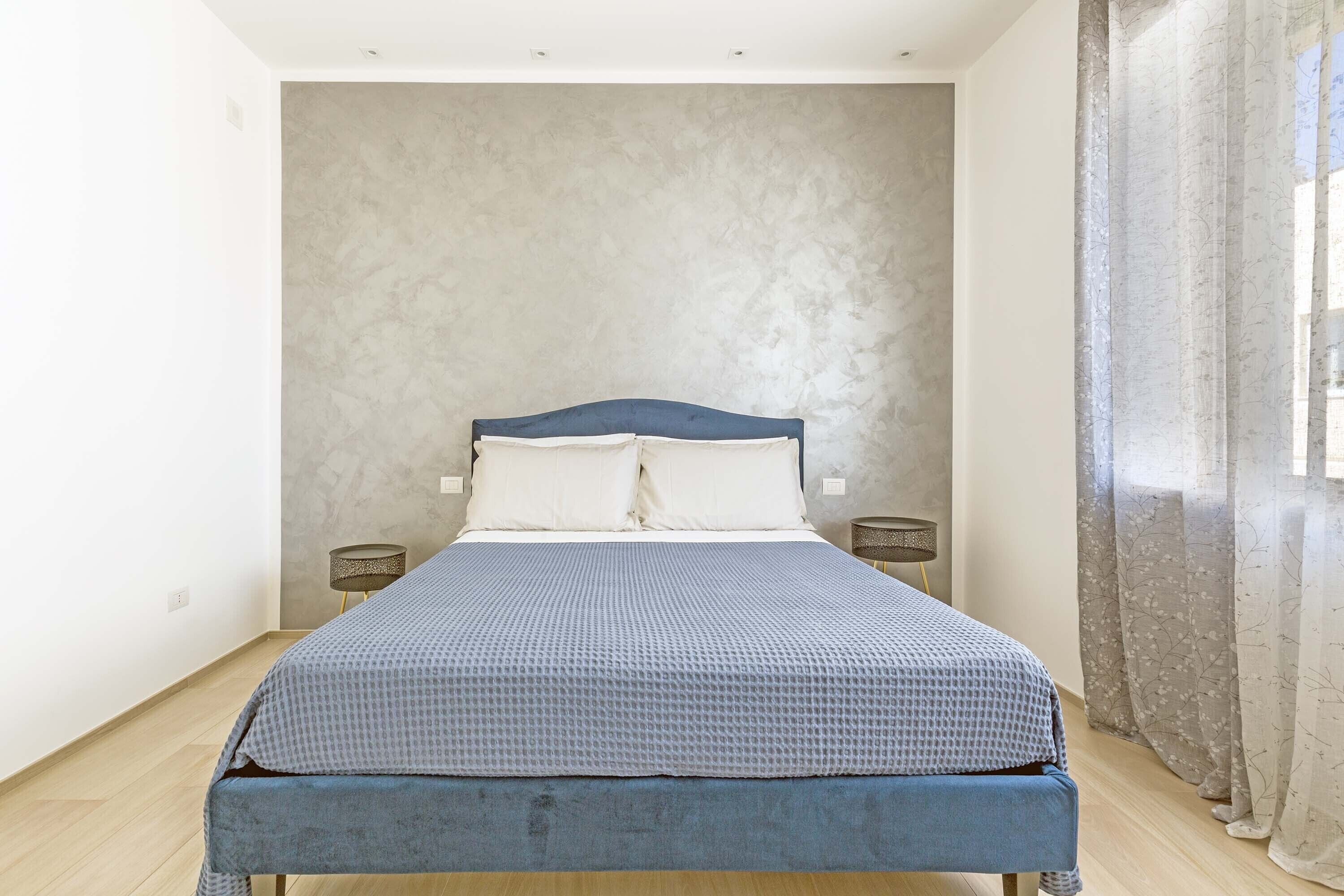 A bedroom with a bed, two bedside tables, and a window with curtains.