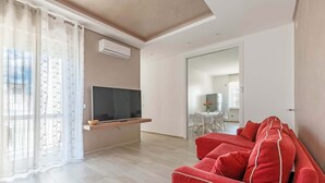 Een moderne woonkamer met een flatscreen televisie, een rode bank en een eethoek op de achtergrond.