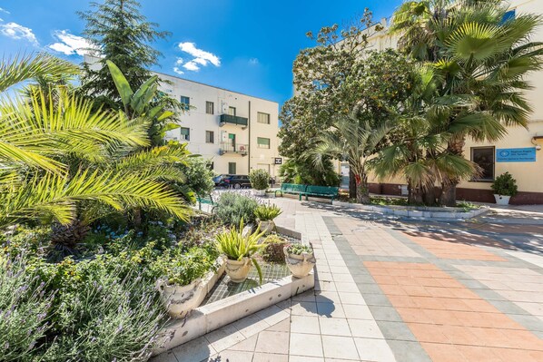 A courtyard with potted plants, a tiled walkway, and a building with balconies.