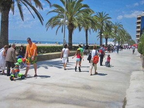 A busy promenade with palm trees, a beach in the background, and people walking. - Holiday apartment with communal pool (Calafell)