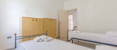 Una habitación con dos camas individuales, un armario y una puerta que da a otra estancia.