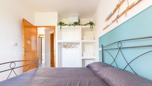 Un dormitorio con cama, armario, estante con ropa colgada y repisa de pared con plantas.
