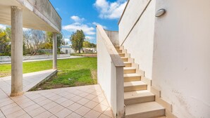 Una escalera conduce a un espacio exterior cubierto con suelo de baldosas y un césped en el fondo.