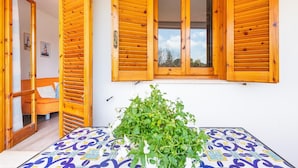 Una habitación con contraventanas de madera, una cama con cabecera naranja y una mesa con mantel estampado.