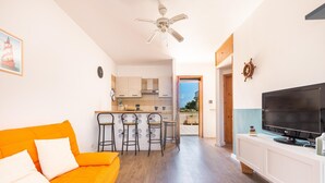 Una sala de estar moderna con un sofá naranja, un televisor y una zona de cocina con taburetes de bar.