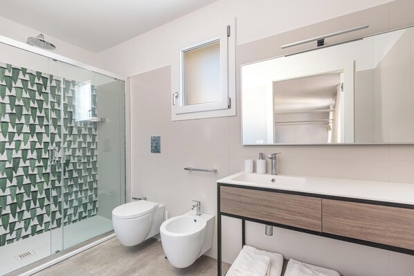 Un baño moderno con cabina de ducha de vidrio, un bidé, un inodoro y un lavamanos con espejo.