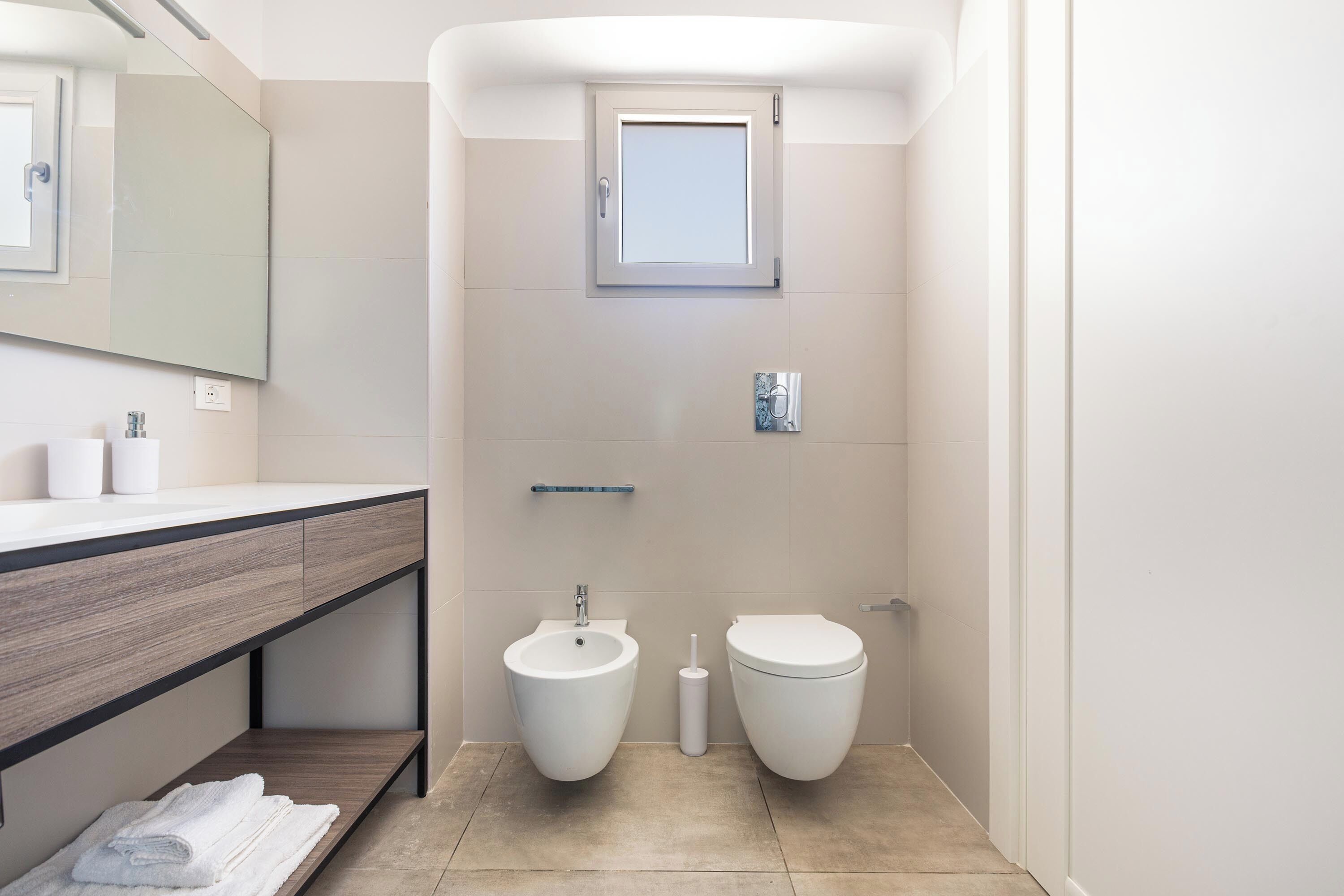 Un baño moderno con bidé, inodoro y tocador con espejo y toallero.