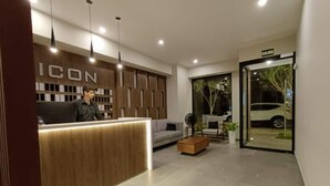 A modern reception area with a wooden reception desk, a sofa, a fan, and a potted plant.