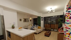 A modern living room with a kitchen area, a sofa, a coffee table, and a TV mounted on the wall.