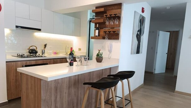 A modern kitchen with a central island, white cabinetry, and a wooden accent wall. There are two black bar stools at the island.