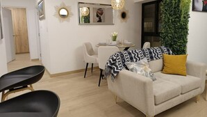 A modern living room with a sofa, a dining table, and chairs. There is a mirror on the wall and a hanging light fixture.