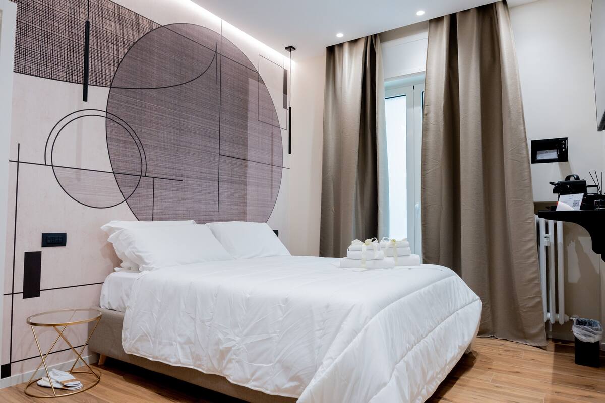 Une chambre d’hôtel moderne avec un grand lit, un élément de décoration circulaire au mur, un bureau avec un ordinateur et une fenêtre avec des rideaux.