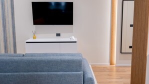 A modern living room with a large flat-screen TV mounted on a white cabinet, a grey sofa, and a wooden floor. - Calvani 23 Luxury House (Bari)