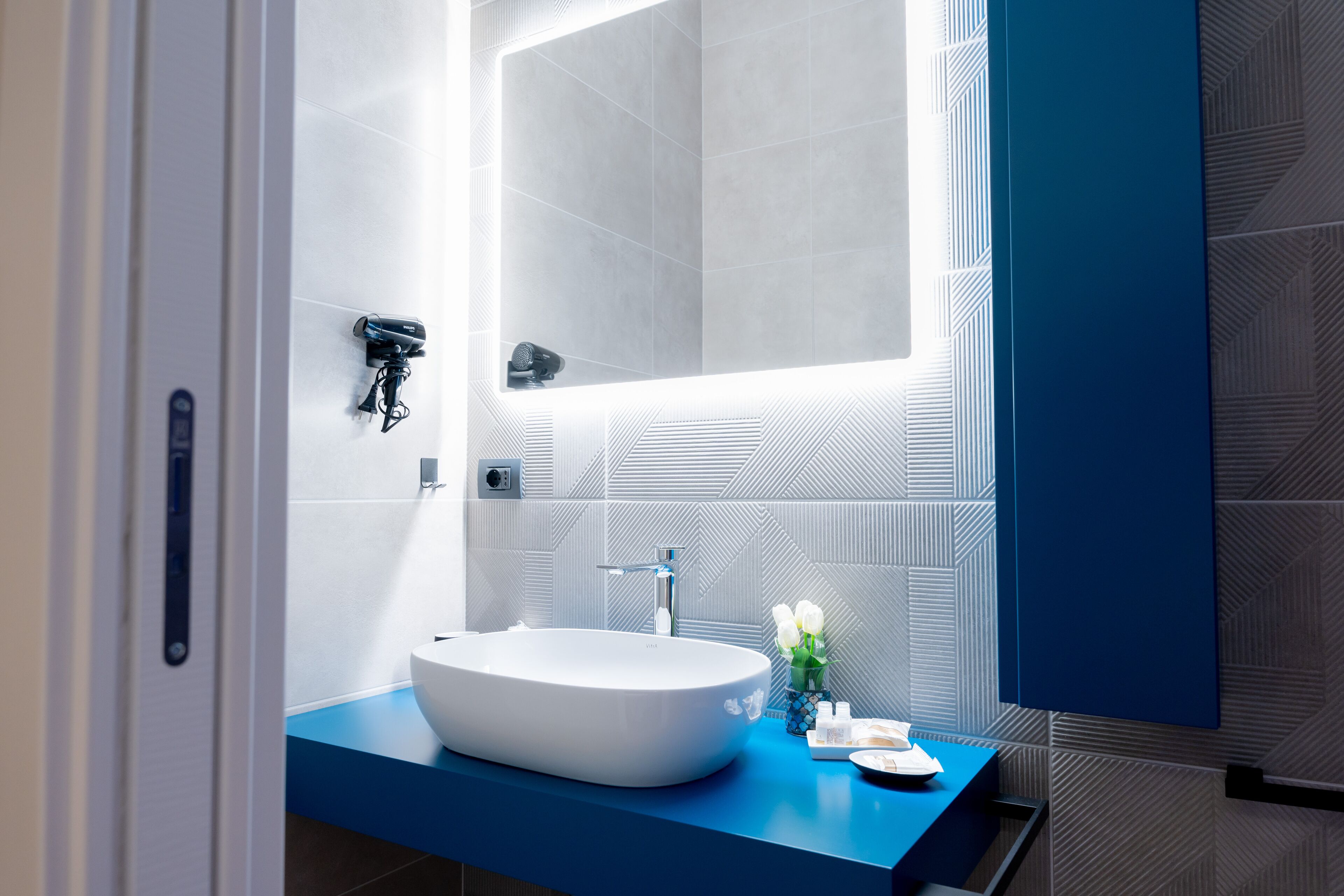 A modern bathroom with a large white sink, a mirror, and a blue countertop.