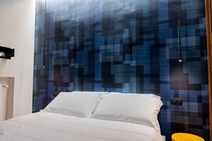 Una habitación de hotel moderna con una cama grande, un muro azul estampado y una mesita de noche amarilla.