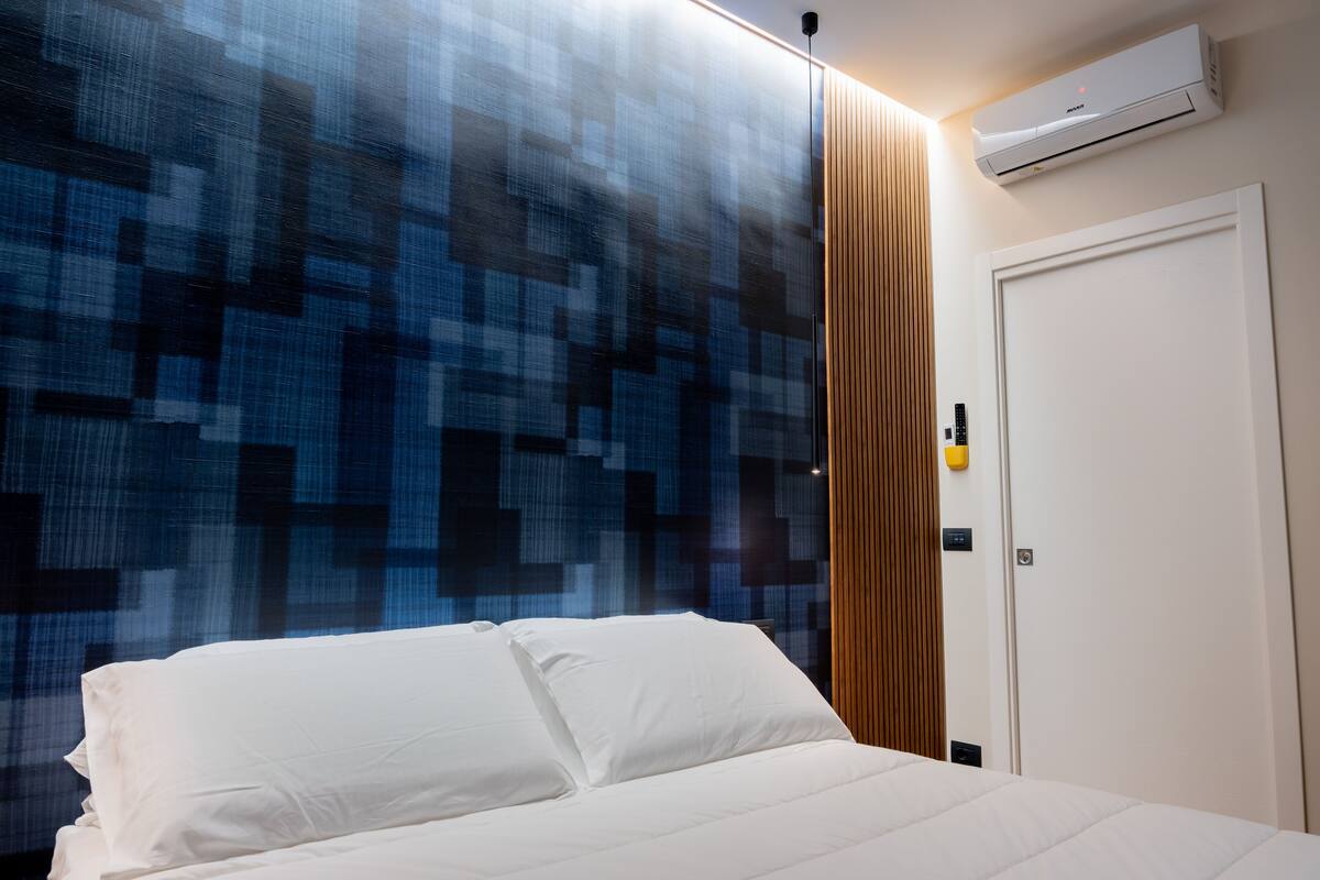 Une chambre d’hôtel avec un lit, un mur orné d’un motif géométrique, un panneau en bois, un appareil de climatisation et une porte.