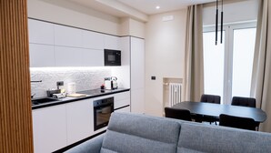 A modern kitchen with white cabinets, a black countertop, and a built-in microwave. There is a dining area with a black table and four chairs. - Calvani 23 Luxury House (Bari)