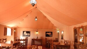 A tented dining area with wooden tables and chairs, a patterned carpet, and artwork on the walls. - Luxury  Saf Saf Camp (Taouz)