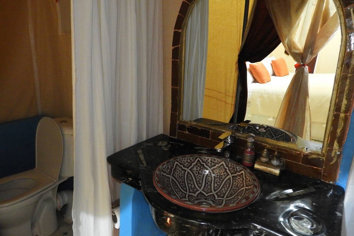 A bathroom with a black marble sink, a decorative bowl, a mirror with a gold frame, and a toilet.
