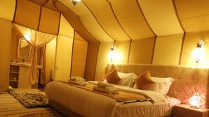 A hotel room with a large bed, a bedside table, a nightstand, a mirror, and a window with curtains. - Luxury  Saf Saf Camp (Taouz)