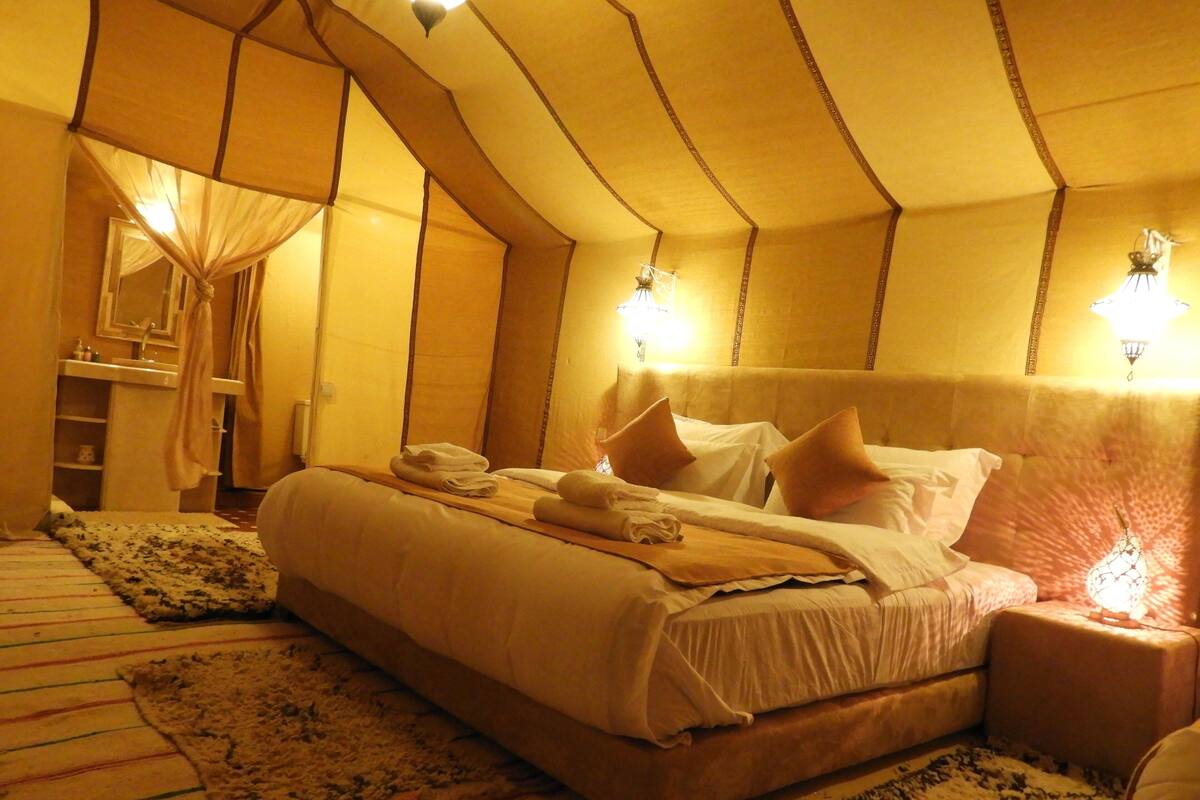 A hotel room with a large bed, a bedside table, a nightstand, a mirror, and a window with curtains.