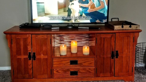 Ein Fernseher auf einer Holzeinrichtung mit Fernbedienung, Tablett und drei brennenden Kerzen.