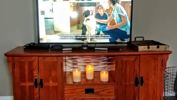 Un téléviseur posé sur un meuble en bois servant de support, avec une télécommande, un plateau et trois bougies allumées.