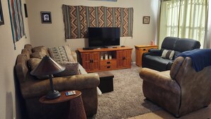 Ein Wohnzimmer mit Fernseher, zwei Ledersofas, einer Holz-Unterhaltungseinheit und einem Wandbehang mit Muster.