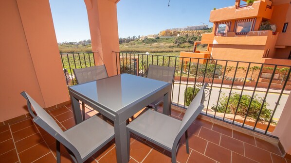 A balcony with a table and chairs, offering a view of a residential area and a distant hill. - Los Hidalgos Golf 6D2 (Manilva)