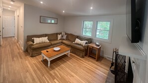 Ein Wohnzimmer mit Ecksofa, Couchtisch aus Holz, Wandfernseher und Kamin.