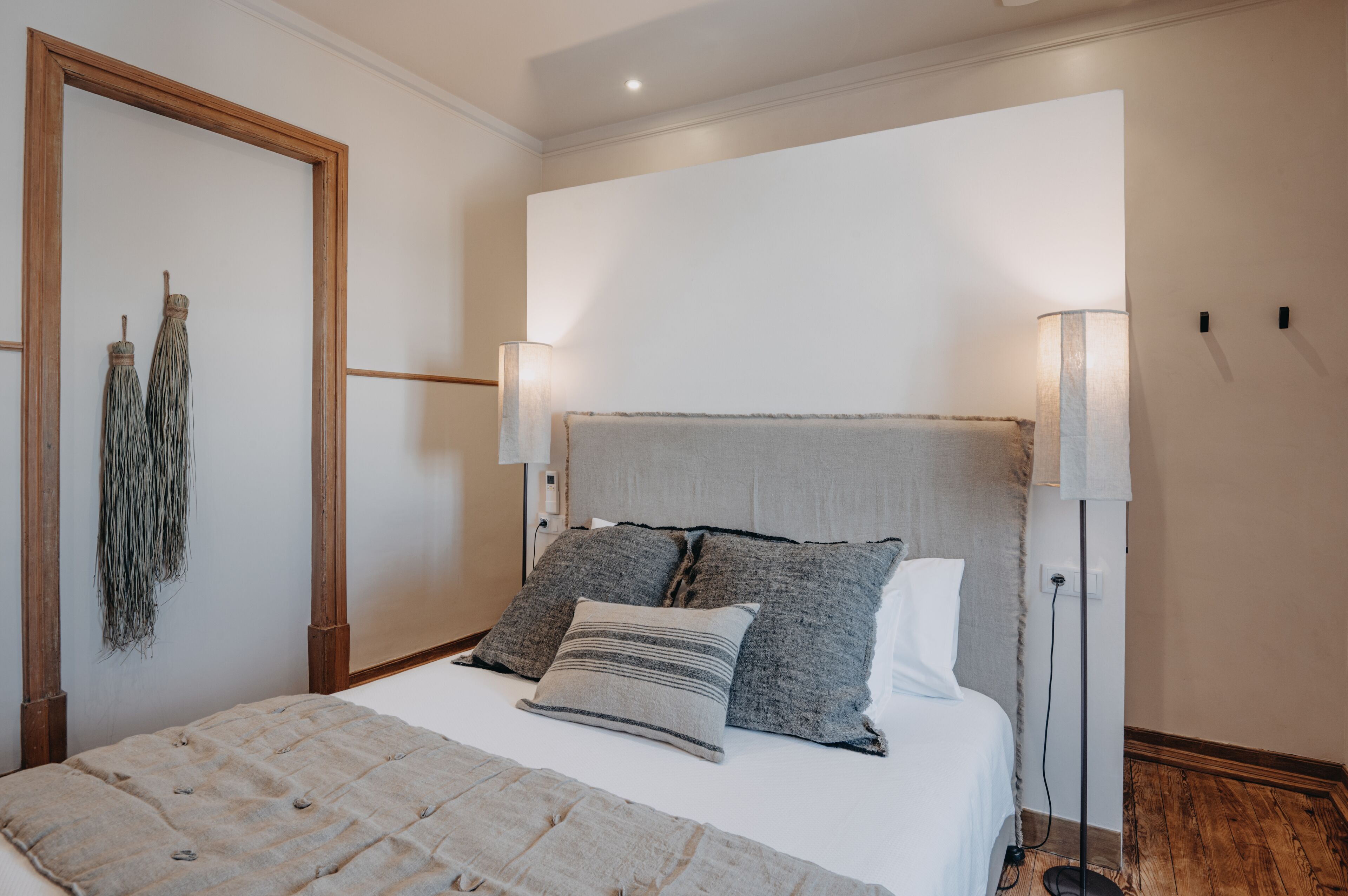 A neatly arranged bedroom with a bed, two bedside lamps, and a wall-mounted mirror.