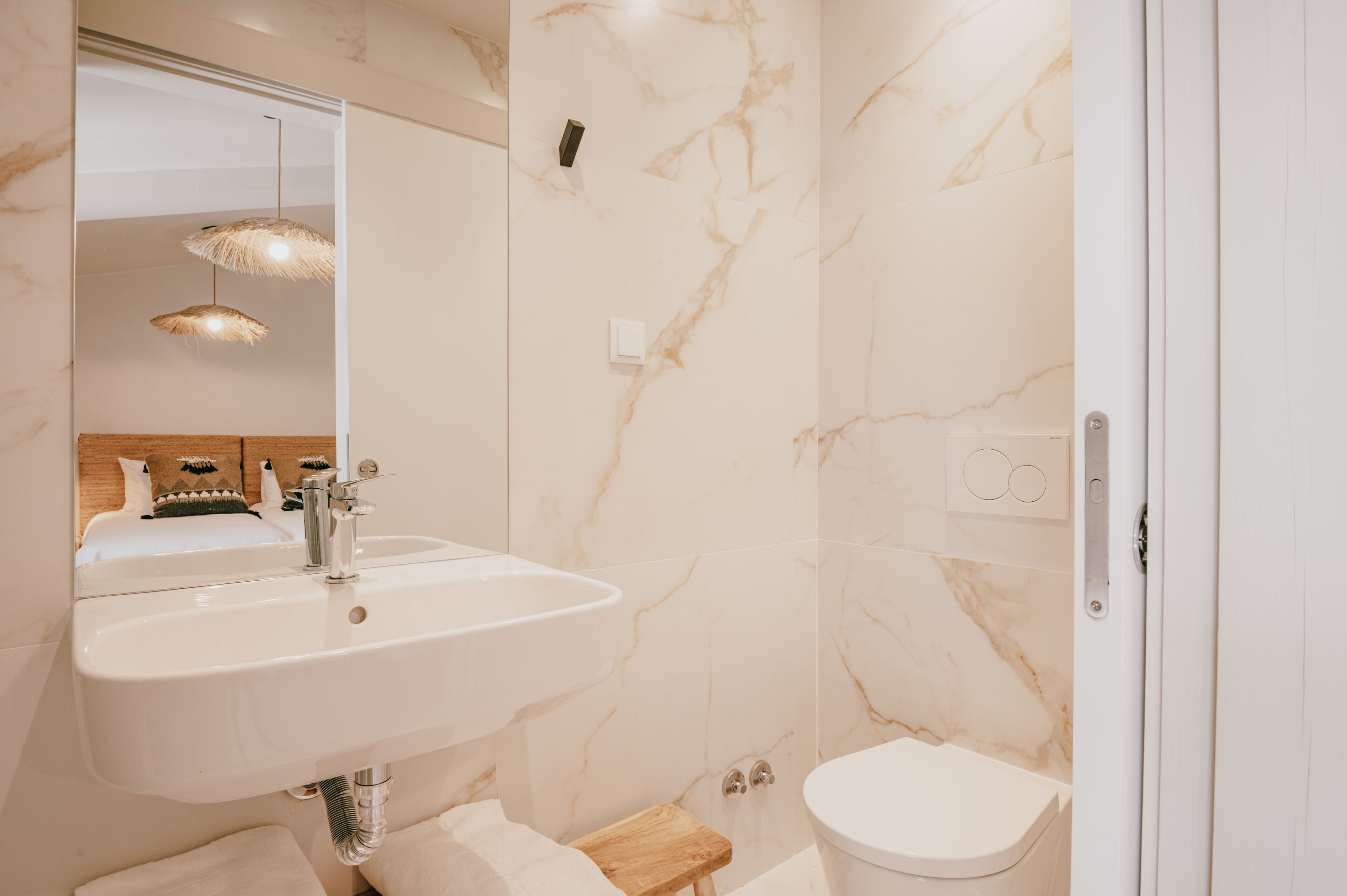 Un bagno con una parete in marmo, un lavandino, un WC e uno sgabello di legno.