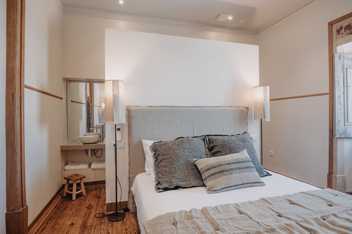 A bedroom with a bed, bedside lamps, a nightstand, a mirror, and a wooden floor.