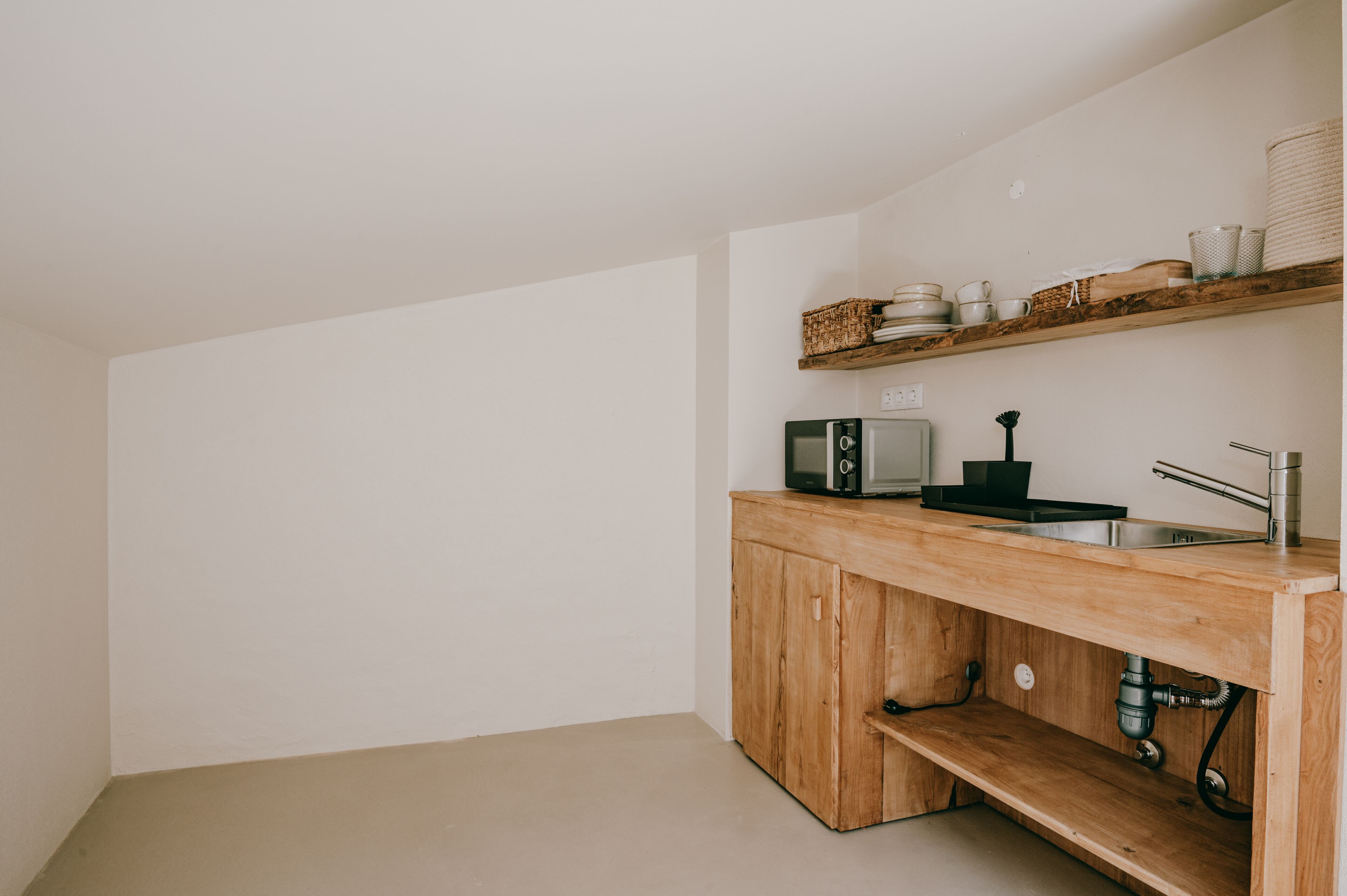 Eine minimalistische Küche mit Holzschränken, einer integrierten Spüle und einer Mikrowelle.