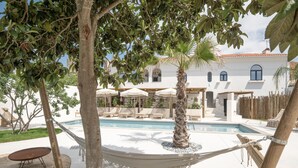 A pool area with lounge chairs and umbrellas, surrounded by trees and a white building with arched windows. - Casa Az-Zagal (Sousel)