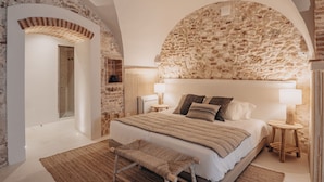 A bedroom with a stone wall, a bed with a quilt, two bedside lamps, and a bench. - Casa Az-Zagal (Sousel)