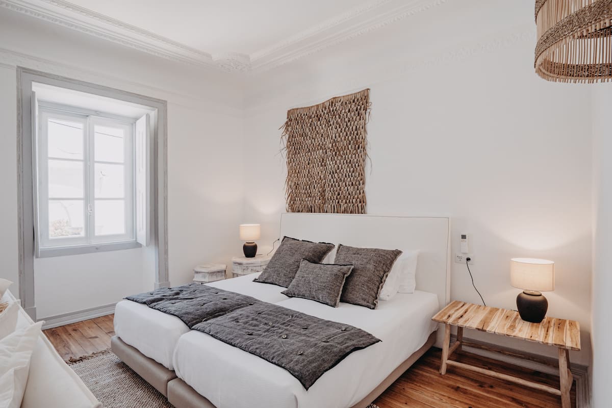 A bedroom with a large bed, bedside tables, a woven wall hanging, and a hanging light fixture.