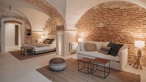 A modern interior with a brick wall, a white sofa, a bed, and a round ottoman. - Casa Az-Zagal (Sousel)
