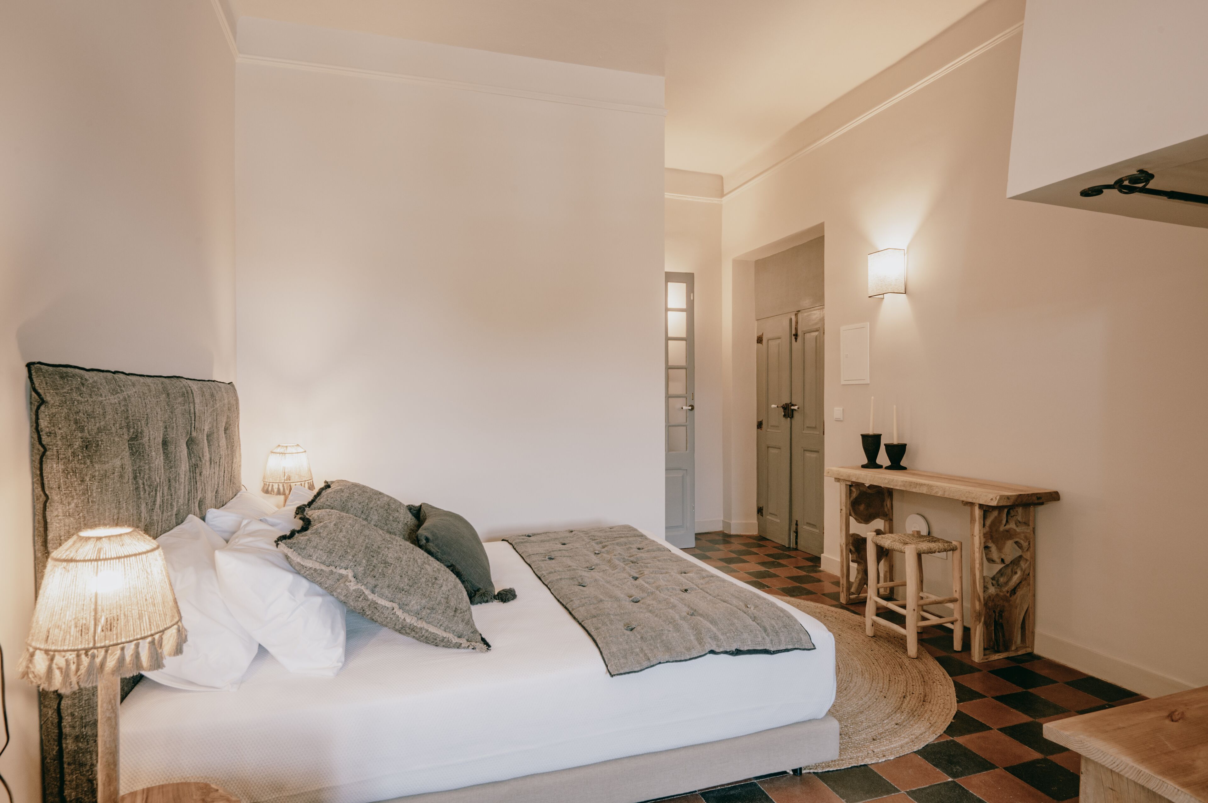 A bedroom with a bed, bedside lamps, a wooden headboard, a bedside table with a lamp, and a checkered floor.