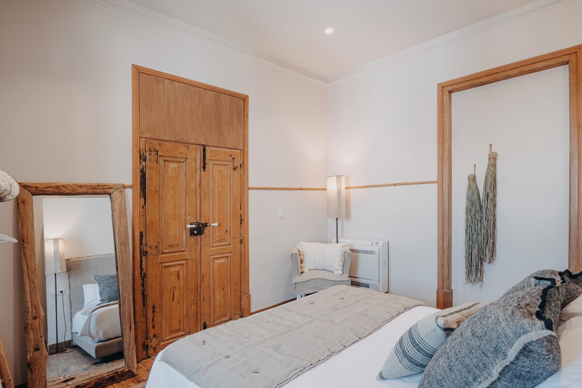 Un dormitorio con un armario de madera, una cama con almohadas, una mesita de noche, una lámpara y una decoración de macramé en la pared.