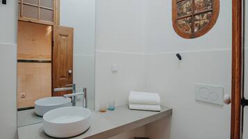 Un baño con dos lavamanos redondos, una puerta de madera, un espejo y un ventanal decorativo.