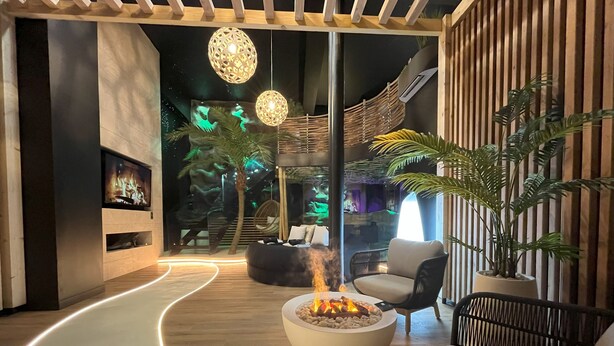 Un espace de détente moderne doté d’un plancher en bois incurvé, d’un foyer central, de sièges et de luminaires sphériques suspendus.